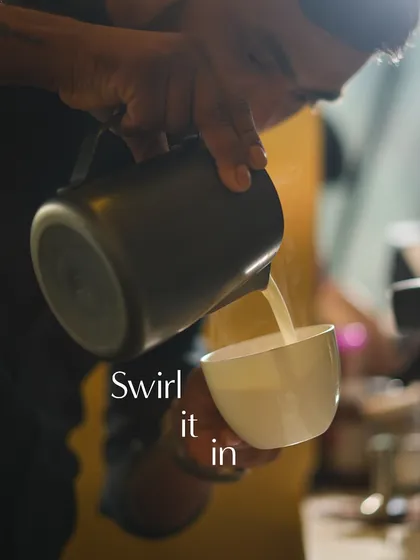 The art of the pour. My barista carefully swirls the frothed milk into the espresso to create intricate latte art.