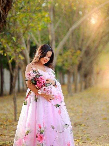 A gentle and beautiful portrait of the mother-to-be holding a bouquet of pink flowers, matching her stunning hand-painted gown.