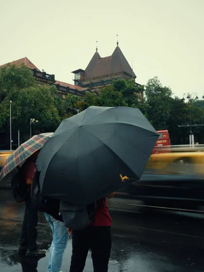 Two people stand under umbrellas as a taxi blurs past them. This use of motion blur highlights the contrast between a shared, static moment and the fast-paced city life around them.