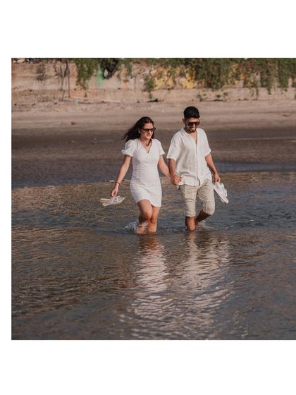 A fun, candid shot of the couple wading through the water, shoes in hand. It captures the playful and carefree spirit of a beach day.