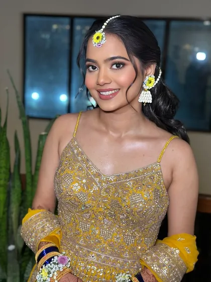 A bright and happy bride. Her makeup is fresh and minimal, letting her natural glow and the vibrant colors of her Haldi ceremony shine.