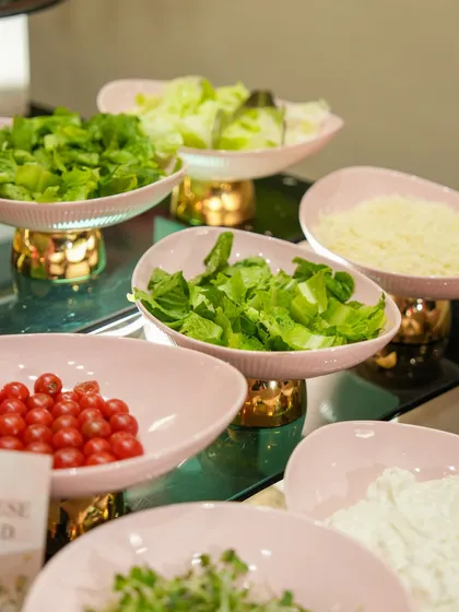A fresh salad bar with ingredients like cherry tomatoes, lettuce, and parmesan cheese, all presented in beautiful pink and gold serving bowls.