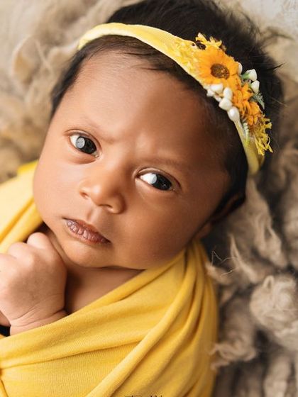 A beautiful, direct gaze from this alert newborn. The yellow sunflower headband perfectly complements her bright and curious expression.