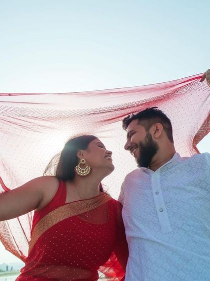 Using the bride's red dupatta to frame the shot, I created a playful and romantic image. The bright sunlight filtering through the fabric gives the photo a warm, happy glow, perfect for a pre-wedding memory.