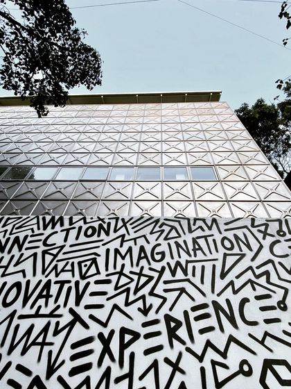 A low-angle shot of the MAP facade, juxtaposing the geometric steel panels with the expressive graffiti-style art on the boundary wall.