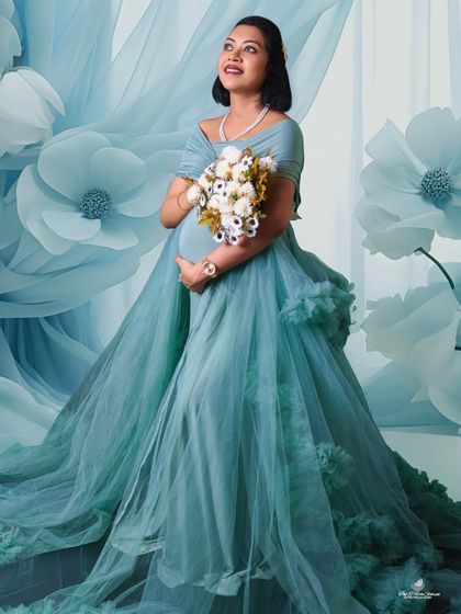 A bright and ethereal solo shot. The mom-to-be is surrounded by large, paper flowers, creating a whimsical and artistic background for her beautiful portrait.