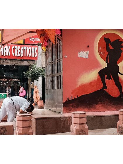 A man bows in prayer on the street in front of a vibrant mural of the Hindu deity Hanuman. This image is a powerful depiction of everyday faith found in the public spaces of Delhi.