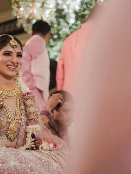 The bride's radiant smile during the wedding rituals, surrounded by the soft hues of her pink lehenga and floral decor.