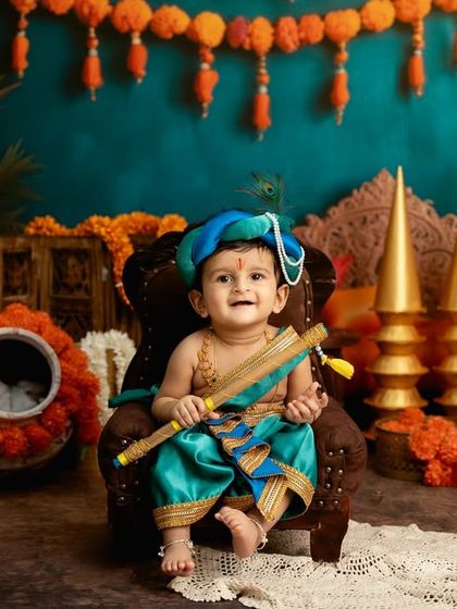 This Little Krishna is full of smiles, sitting in a festive setting decorated with marigold flowers.