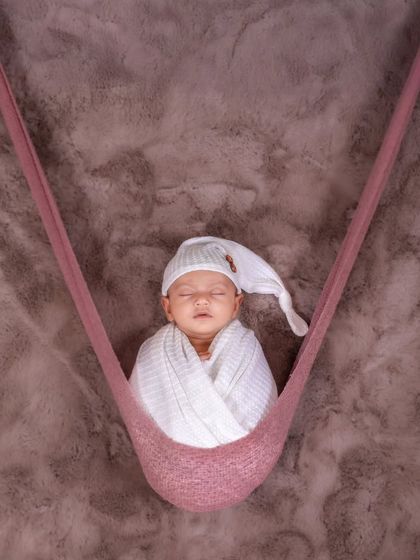Gently swaying in a soft hammock, this swaddled newborn looks perfectly content. This hanging prop adds a unique and dreamy element to the portrait session.