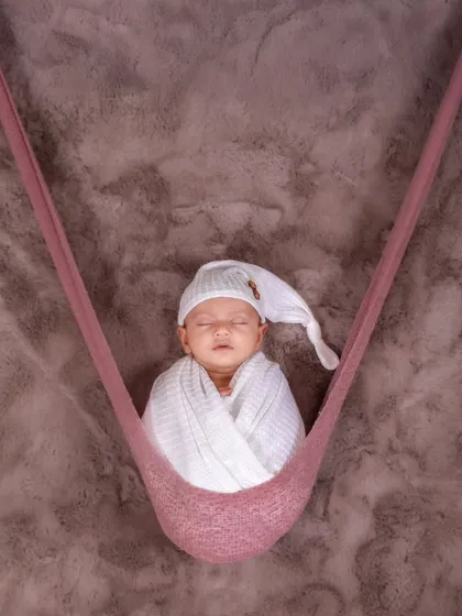 A baby sleeps soundly while suspended in a soft pink hammock. This pose is always a parent favorite, showing the baby safe and snug.