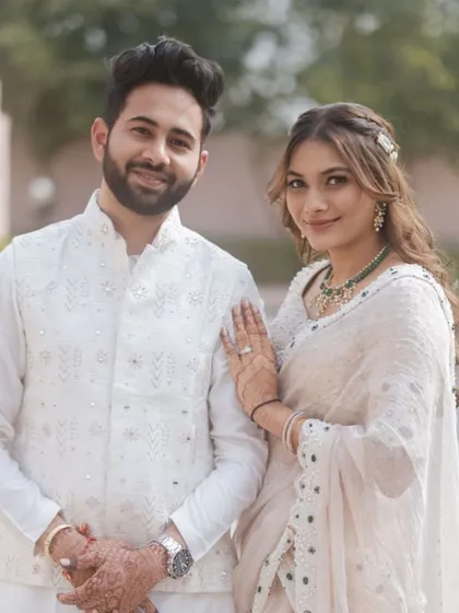 The couple posing together, looking perfectly coordinated in their white outfits. The bride's makeup is fresh and minimal.