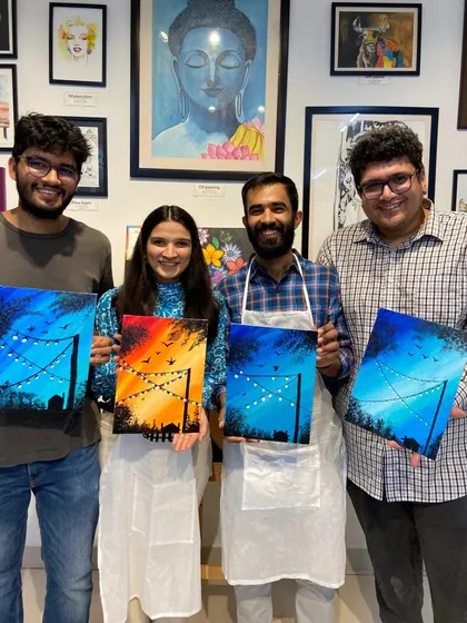 A group of friends with their finished canvas paintings of night skies. It's amazing to see how each person adds their own unique touch to the same theme.