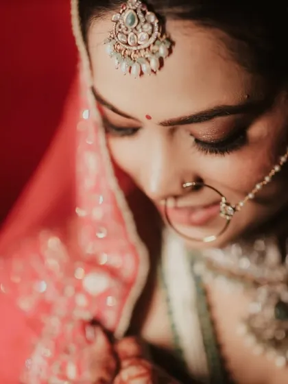 A close up of the bride, Riya, looking down with a gentle smile. This shot focuses on her intricate nath and maang tikka, key elements of her bridal shringaar.