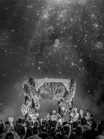 The night sky explodes with fireworks as Deeksha and Prakhar stand under the mandap. This black and white version emphasizes the dramatic contrast and epic scale of the celebration.