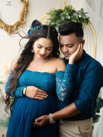 An intimate close-up of the couple, highlighting the delicate lace details of the blue gown. The soft focus is on their connection and the gentle touch on the baby bump.