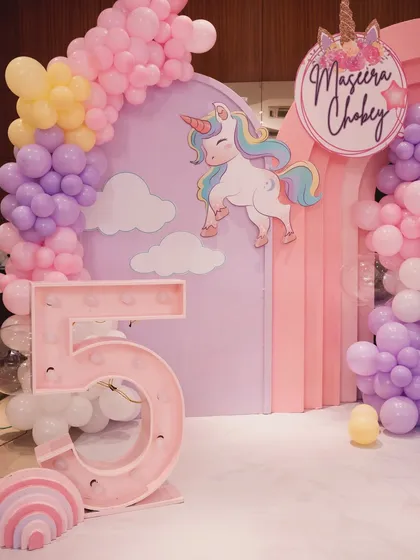 A close-up of the unicorn-themed decor, featuring a marquee number '5' and a personalized sign for Maseera Chobey.