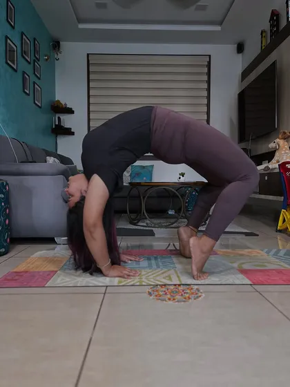 A student holding a strong Urdhva Dhanurasana, or upward bow pose, in her living room. The ability to practice at home is one of the greatest gifts of yoga.