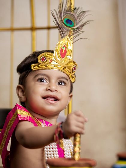 A joyful shot of a little boy in his Krishna outfit, holding a prop. His happy expression is the centerpiece of this festive portrait.