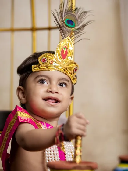 A joyful shot of a little boy in his Krishna outfit, holding a prop. His happy expression is the centerpiece of this festive portrait.