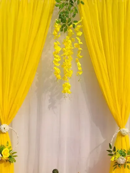 A minimalist yet elegant Ganpati backdrop. The focus here is on the beautiful yellow drapes and the hanging floral arrangement in the center, creating a serene and graceful space to place the idol.