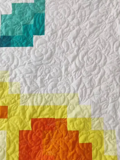 A detail shot of another pixelated rose quilt, this one in a warm sunset palette of yellow, orange, and teal.