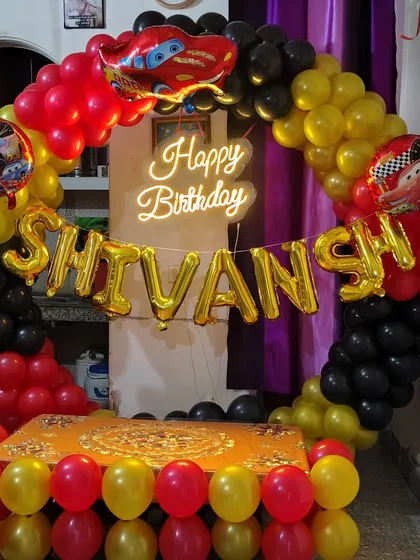 A high-speed "Cars" themed birthday party. This setup features a full balloon ring in the movie's signature red, yellow, and black colors, a neon "Happy Birthday" sign, and Lightning McQueen foil balloons.