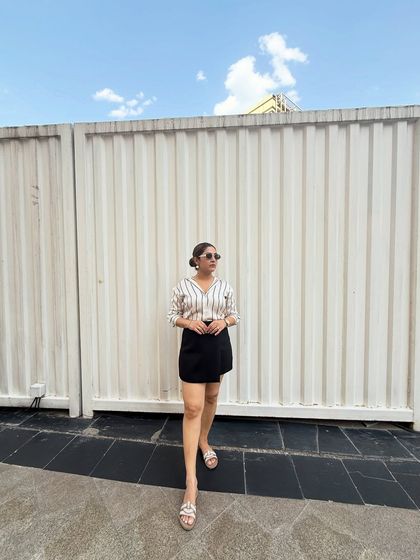 This chic outfit, featuring a striped satin shirt and a black skort, is a perfect example of a smart casual look that can take you from a brunch meeting to a day of shopping.