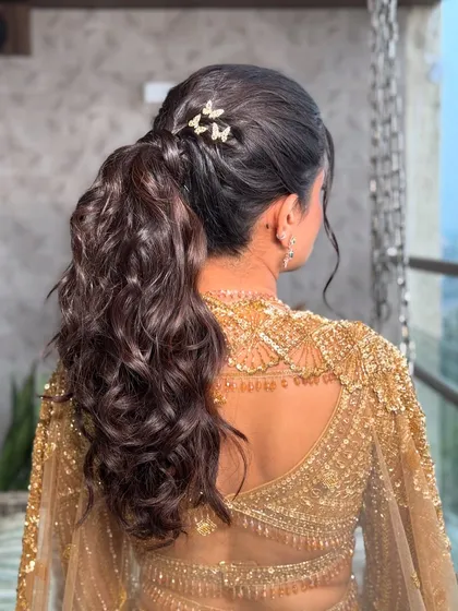 A chic and modern ponytail with soft curls and butterfly clips. This hairstyle is perfect for a sangeet or reception, adding a touch of playful elegance.