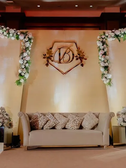 An elegant reception stage that exudes timeless class. The design features a clean, neutral backdrop with two large floral walls and a custom monogram, creating a sophisticated and personalized photo point.