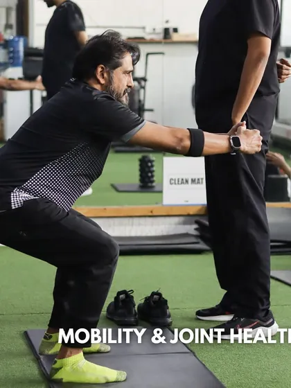 We emphasize mobility and joint health for long-term wellness. A coach assists a client with a squat variation, ensuring they move through a full, pain-free range of motion to improve function.