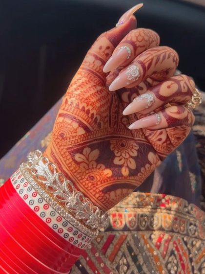 A stunning close-up of wedding nails designed to complement traditional henna and bridal bangles. The delicate white floral art and subtle sparkle add a touch of modern elegance.