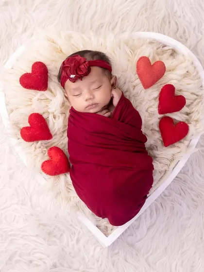 All you need is love. A newborn wrapped in red, surrounded by hearts, makes for a perfect and adorable portrait.
