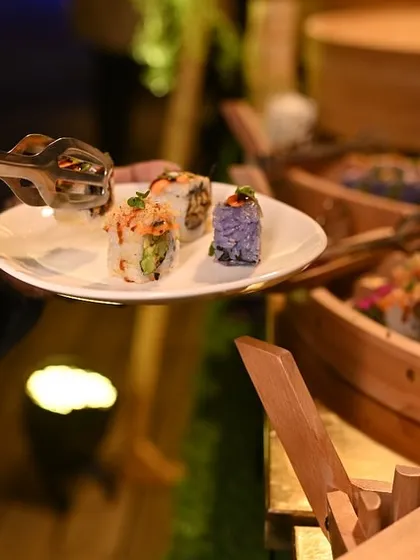 A guest helps themselves to freshly made sushi from our live station, where rolls are presented in charming wooden sushi boats.