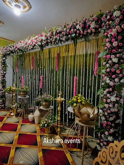 An elegant naming ceremony setup with a backdrop of hanging jasmine garlands. The stage is decorated with brass lotus stands and a traditional lamp, creating a serene and beautiful ambiance.