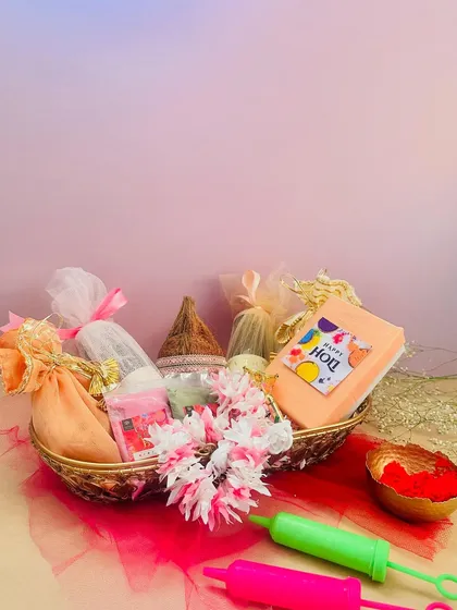 A simple and sweet Holi hamper in a gold wire basket. It contains everything you need for the ritual, including a coconut, floral garland, and organic colors.