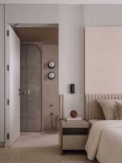The father's bedroom is a composed sanctum of beige tones, fluted walls, and wooden paneling. The design connects seamlessly to the en-suite bathroom, creating a private suite that is both masculine and serene.