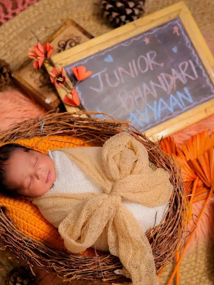 A newborn peacefully sleeping in a nest-like basket, swaddled in earthy tones. The chalkboard with the baby's name adds a lovely personal touch.