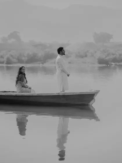 A serene and atmospheric black and white photo of the couple in a boat on calm water. This minimalist and artistic shot has a timeless, film-like quality.