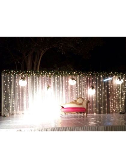 A minimalist night reception stage set against a dark backdrop. The curtain of fairy lights and hanging orb lights creates a simple, starry effect, focusing all the attention on the couple's seating.
