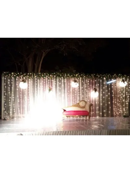 A minimalist night reception stage set against a dark backdrop. The curtain of fairy lights and hanging orb lights creates a simple, starry effect, focusing all the attention on the couple's seating.