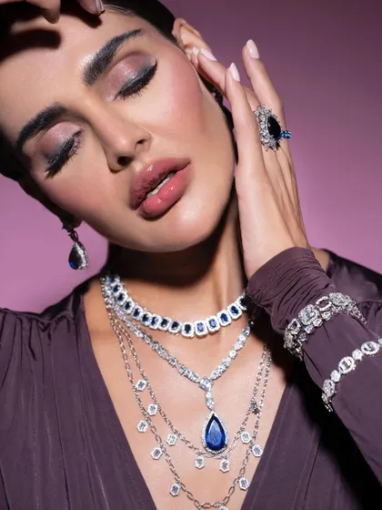 A serene and luxurious portrait showcasing a layered sapphire and diamond necklace set. The styling emphasizes elegance, with closed eyes drawing attention to the makeup and the brilliance of the jewels.