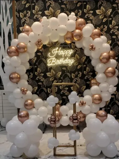 An elegant white and rose gold balloon ring with a neon sign, set against a patterned wallpaper.