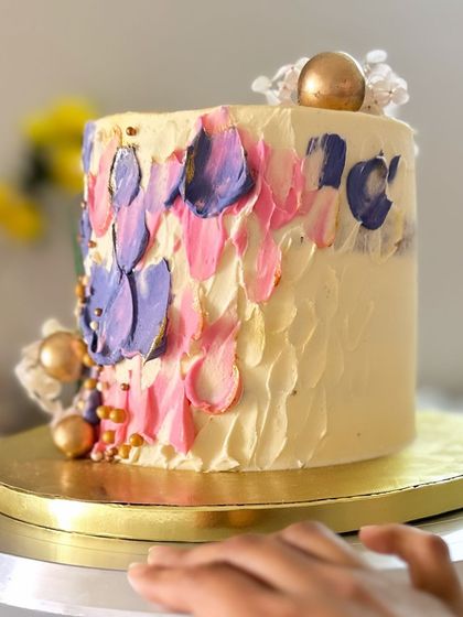 This tall cake features a beautiful palette-knife painting effect with strokes of pink and purple buttercream, accented with gold leaf. It’s an edible piece of art, perfect for a stylish celebration.