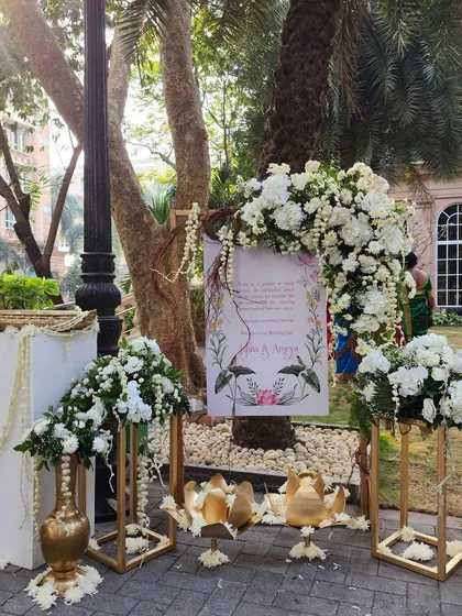 A charming welcome corner at an outdoor wedding, featuring a personalized sign, golden lotus props, and beautiful arrangements of white flowers.