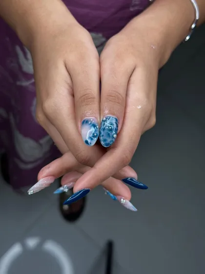 It's all in the details. This stunning blue marble and chrome nail set, complete with delicate rhinestone accents, showcases the advanced artistry our students learn.