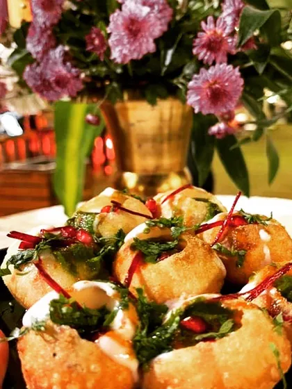 A close-up of beautifully prepared Dahi Puri, filled with delicious toppings and garnished with pomegranate seeds and fresh herbs.