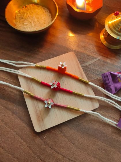 These delicate floral rakhis are handmade with thread and small beads. They come in a variety of warm colors like orange, pink, and red.