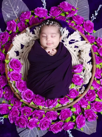 A smiling newborn swaddled in purple, surrounded by a wreath of matching flowers. We love it when we catch these fleeting smiles.