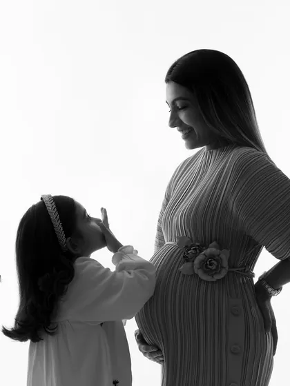 A sweet kiss for the baby bump. This black and white silhouette captures a tender moment between a girl and her expectant mother, creating a timeless piece of art.
